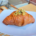 Croissant Sicilia pe farfurie cu cremă de vanilie și portocală confiată, cu fistic mărunțit deasupra, la Pain Plaisir